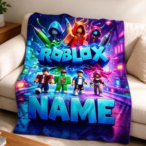 May include: A rectangular fleece blanket featuring a vibrant Roblox graphic with multiple block-style characters, neon blue and purple city background elements, and the text ROBLOX and NAME in large, bold, three-dimensional blue lettering.