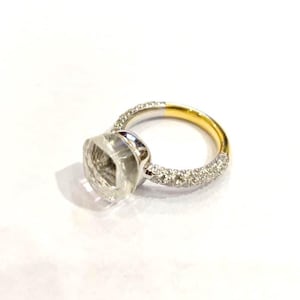 May include: A silver and gold ring with a large, clear, faceted gemstone. The band is silver with small, clear stones set around the top half. The bottom half of the band is gold.