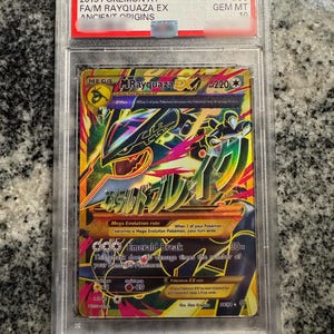 Puede incluir: Una carta Pokémon calificada con Mega Rayquaza EX del set 2015 XY Ancient Origins. La carta tiene un diseño colorido con detalles dorados, verdes y negros. La carta está dentro de un soporte protector con una etiqueta roja.