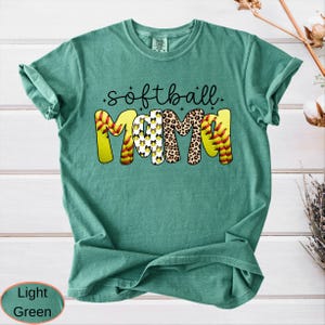 May include: Light green t-shirt with the words "softball mama" in a playful design. The word "mama" is decorated with a softball, leopard print, and softball patterns. The shirt is a comfortable, casual style.