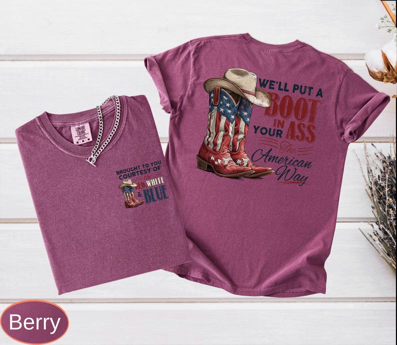 May include: Two berry-colored t-shirts. One shirt has a small graphic of a cowboy boot with the text "BROUGHT TO YOU COURTESY OF WHITE & BLUE". The other shirt features a graphic of a cowboy boot with the American flag and the text "WE'LL PUT A BOOT IN YOUR ASS The American Way".
