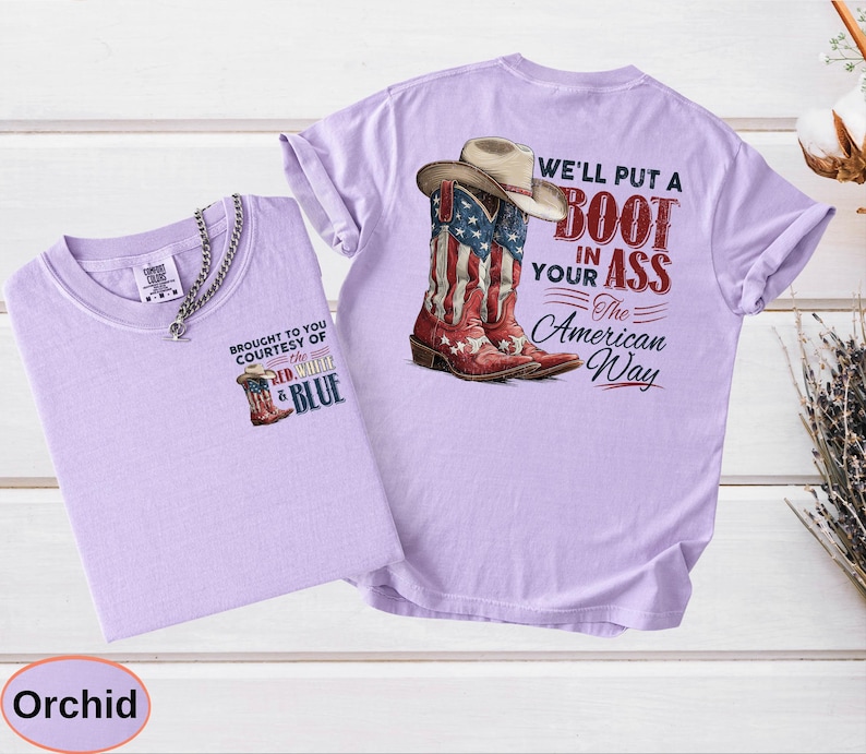 May include: Orchid-colored t-shirts with a cowboy boot graphic. One shirt features a small boot graphic and text, "BROUGHT TO YOU COURTESY OF THE RED, WHITE & BLUE." The other shirt has a larger graphic of a cowboy boot with a hat and the text, "WE'LL PUT A BOOT IN YOUR ASS The American Way."