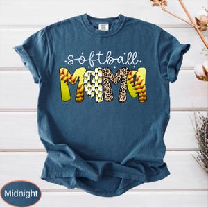May include: A navy blue t-shirt with the words "softball Mama" in white script and a colorful design. The word "Mama" features a softball design, leopard print, and a pattern of softballs. The shirt is a comfortable, casual style.