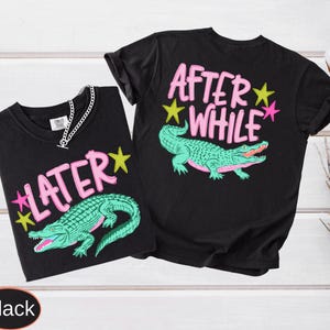 Puede incluir: Dos camisetas negras con dise&ntilde;os a juego. Cada camiseta presenta un gr&aacute;fico de caim&aacute;n turquesa con las palabras "LATER" y "AFTER WHILE" en rosa, acentuadas con estrellas amarillas y rosas. Una camiseta tiene una cadena plateada.