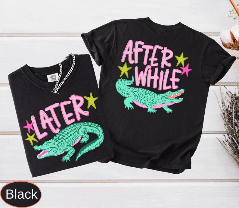 Puede incluir: Dos camisetas negras con dise&ntilde;os a juego. Cada camiseta presenta un gr&aacute;fico de caim&aacute;n turquesa con las palabras "LATER" y "AFTER WHILE" en rosa, acentuadas con estrellas amarillas y rosas. Una camiseta tiene una cadena plateada.