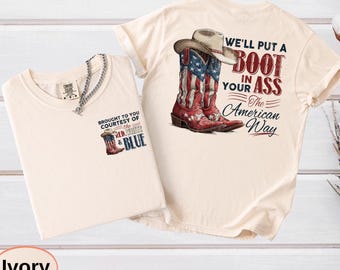 May include: Two ivory-colored t-shirts. One shirt features a graphic of a cowboy boot with the American flag design and the text "BROUGHT TO YOU COURTESY OF the RED, WHITE & BLUE". The other shirt has a cowboy boot and hat graphic with the text "WE'LL PUT A BOOT IN YOUR ASS The American Way".
