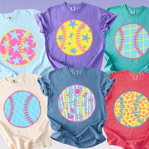 May include: A collection of six short-sleeved t-shirts in various colors, each featuring a baseball-themed graphic. The designs include stars, baseball stitching, and other summer-themed elements. The shirts are in light blue, purple, teal, beige, blue, and red.