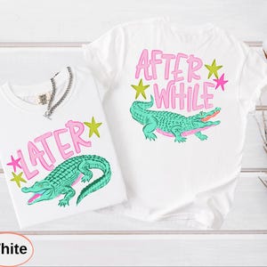 Puede incluir: Dos camisetas blancas con dise&ntilde;os a juego. Cada camiseta presenta una ilustraci&oacute;n de un caim&aacute;n verde y las frases "LATER" y "AFTER WHILE" en texto rosa con acentos de estrellas amarillas y rosas. Una cadena de plata est&aacute; en una camiseta.