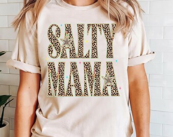 May include: A cream-colored short-sleeve t-shirt featuring the text SALTY MAMA in a bold, leopard print pattern. The letters are outlined in a light green border and accented with small, colorful star shapes and two larger star icons.