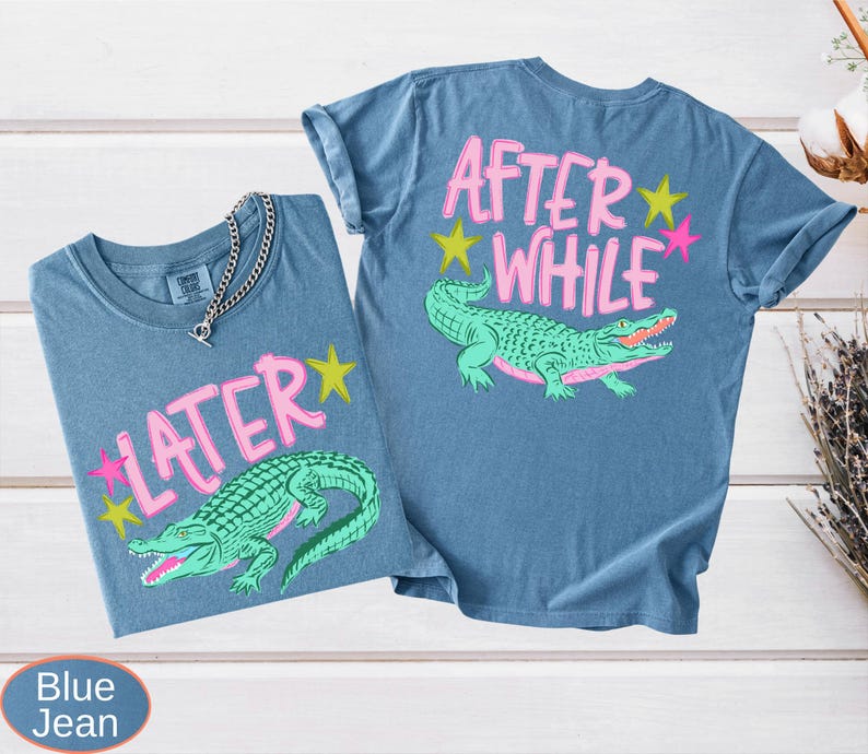 Puede incluir: Dos camisetas azul vaquero con un gr&aacute;fico de un caim&aacute;n verde y el texto "LATER" y "AFTER WHILE" en rosa. El caim&aacute;n tiene la boca roja y est&aacute; rodeado de estrellas rosas y amarillas. Una cadena de plata est&aacute; en una camiseta.