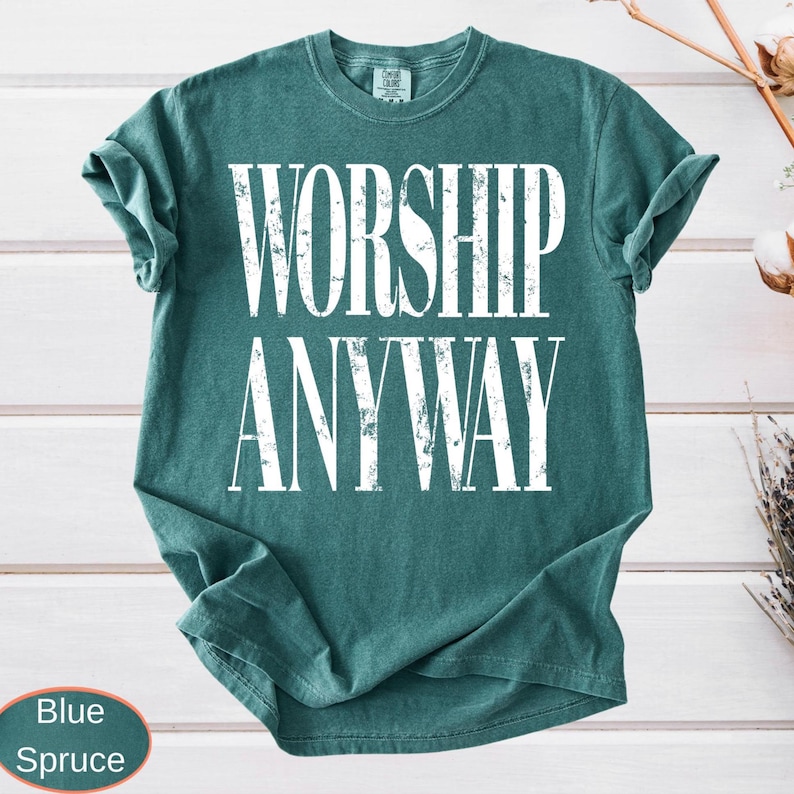 A high-quality graphic design featuring the bold, distressed text "WORSHIP ANYWAY" in a vintage grunge style, meant for a garment-dyed top.