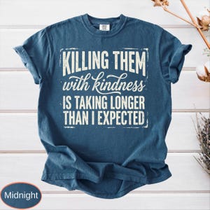 Op de afbeelding: Een nachtblauw t-shirt met korte mouwen en de witte, verweerde tekst "KILLING THEM with kindness IS TAKING LONGER THAN I EXPECTED" in een combinatie van blokletters en cursief lettertype op het midden van de borst.