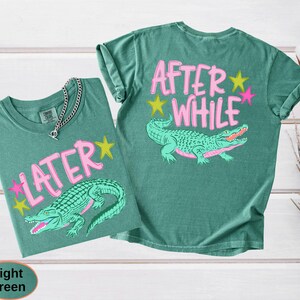 Puede incluir: Dos camisetas verde claro con gr&aacute;ficos de caimanes. Una camiseta dice "LATER" con una fuente rosa y un caim&aacute;n verde. La otra camiseta dice "AFTER WHILE" con una fuente rosa y un caim&aacute;n verde. Ambas camisetas tienen estrellas amarillas y rosas.