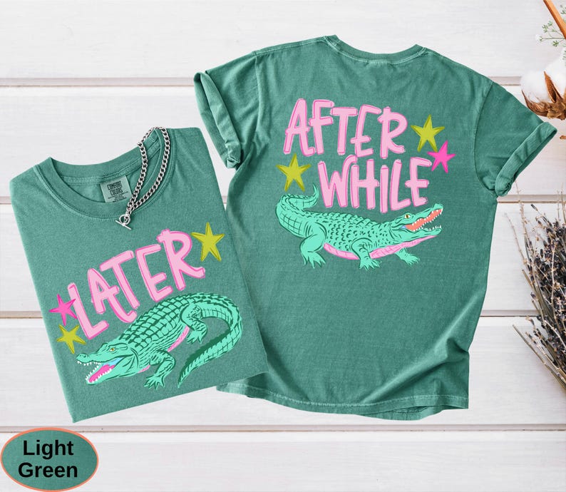 Puede incluir: Dos camisetas verde claro con gr&aacute;ficos de caimanes. Una camiseta dice "LATER" con una fuente rosa y un caim&aacute;n verde. La otra camiseta dice "AFTER WHILE" con una fuente rosa y un caim&aacute;n verde. Ambas camisetas tienen estrellas amarillas y rosas.