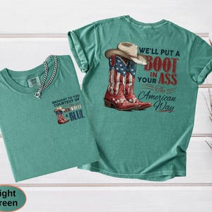 May include: Two light green t-shirts. One shirt has a small graphic of a cowboy boot with the text "BROUGHT TO YOU COURTESY OF RED WHITE & BLUE". The other shirt has a graphic of a cowboy boot and hat with the text "WE'LL PUT A BOOT IN YOUR ASS The American Way".
