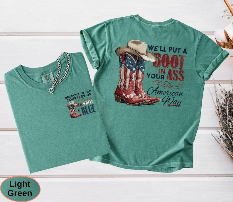 May include: Two light green t-shirts. One shirt has a small graphic of a cowboy boot with the text "BROUGHT TO YOU COURTESY OF RED WHITE & BLUE". The other shirt has a graphic of a cowboy boot and hat with the text "WE'LL PUT A BOOT IN YOUR ASS The American Way".