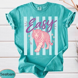 A graphic displaying alternating black and light blue vertical blocks. In the foreground, a pink tiger stands below a large purple "Easy" sign written in a flowing script, surrounded by star embellishments.