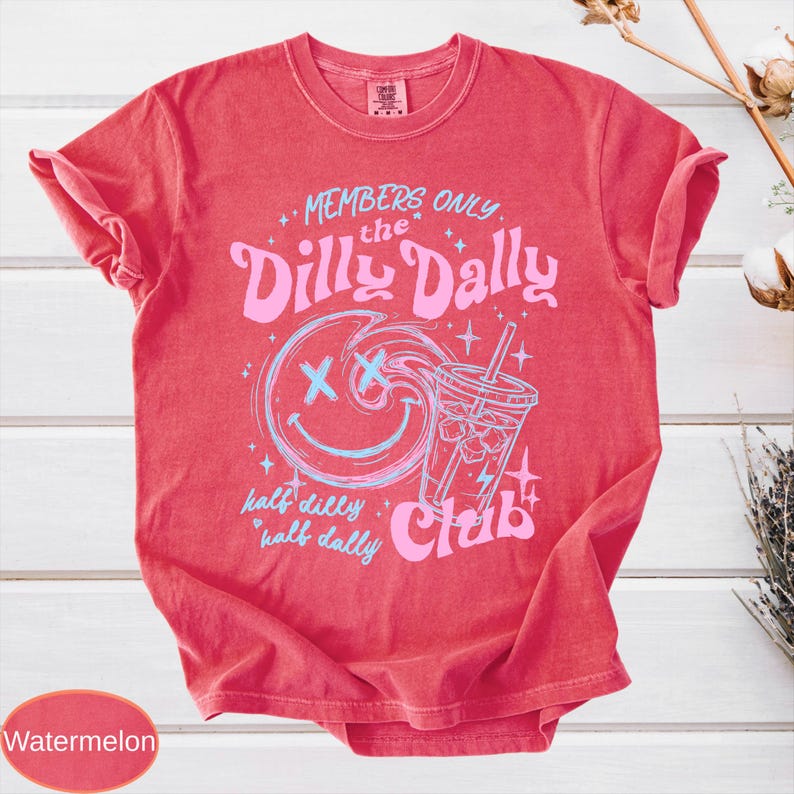 May include: Watermelon-colored t-shirt with a crew neck. The shirt features a graphic design with the text "MEMBERS ONLY the Dilly Dally Club" and a smiling face with an ice drink. The text "half dilly half dally" is also included.