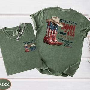 May include: Two moss green t-shirts with graphic designs. One shirt features a cowboy boot with the American flag and the text "BROUGHT TO YOU COURTESY OF WHITE & BLUE". The other shirt has a cowboy boot with the American flag and the text "WE'LL PUT A BOOT IN YOUR ASS The American Way".