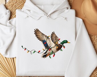 May include: A white hooded sweatshirt featuring a graphic of a mallard duck in flight, wrapped in a string of colorful red, green, and yellow Christmas lights. The duck has brown, white, and iridescent blue wing feathers and a yellow beak.