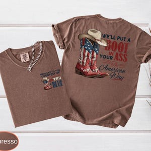 May include: Two espresso-colored t-shirts. One shirt features a small graphic of a cowboy boot with red, white, and blue colors and the text "Brought to you courtesy of Red, White & Blue." The other shirt has a larger graphic of a cowboy boot and hat with the text "We'll put a boot in your ass the American way."