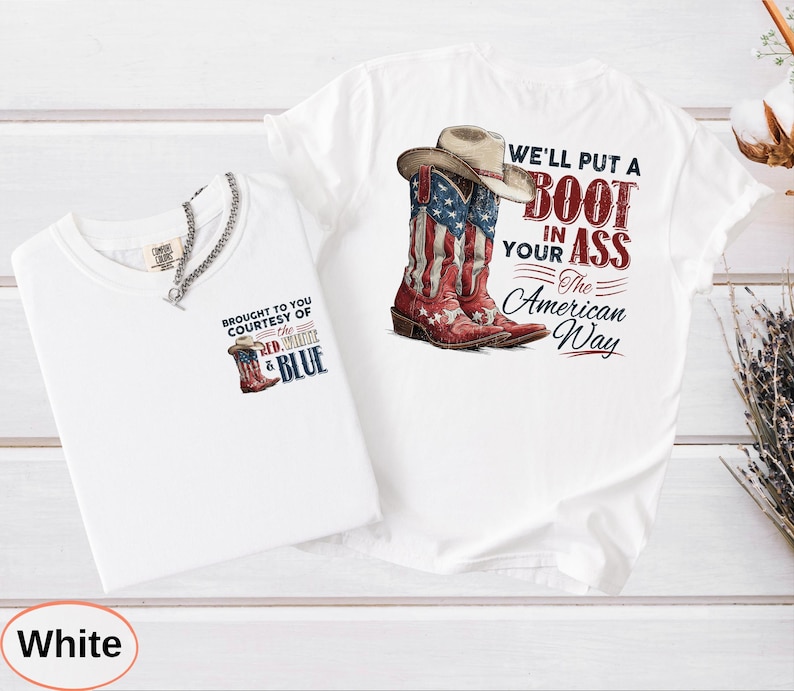 May include: Two white t-shirts. One features a graphic of a cowboy boot with the American flag design and a cowboy hat, with the text "WE'LL PUT A BOOT IN YOUR ASS The American Way." The other shirt has a smaller boot graphic and the text "BROUGHT TO YOU COURTESY OF THE RED, WHITE & BLUE."