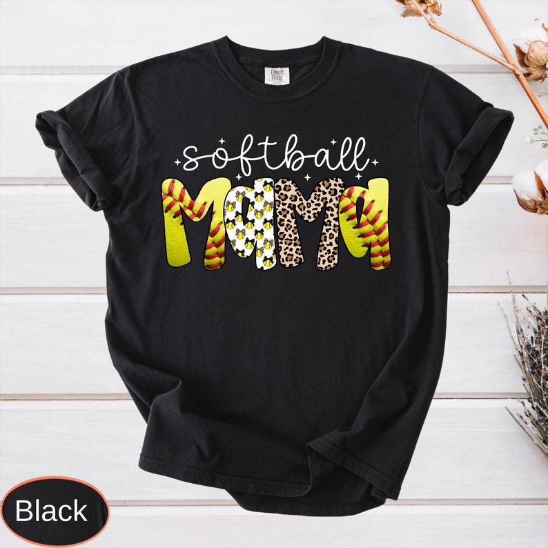 May include: Black t-shirt with the words "softball mom" in white script. The word "MOM" is in yellow, leopard print, and softball design. The shirt is a casual style.