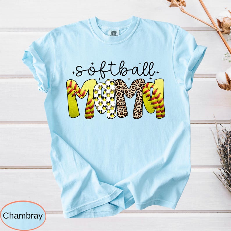 May include: Light blue t-shirt with the words "softball mama" in a playful design. The word "softball" is in black script, and "mama" is in yellow, leopard print, and softball-themed patterns. The shirt is made of a soft material.