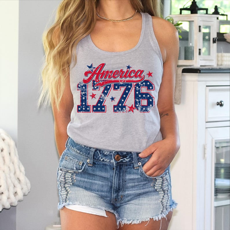 May include: A gray tank top with the text "America 1776" in red and blue. The text has a distressed, vintage look. The tank top is paired with denim shorts.