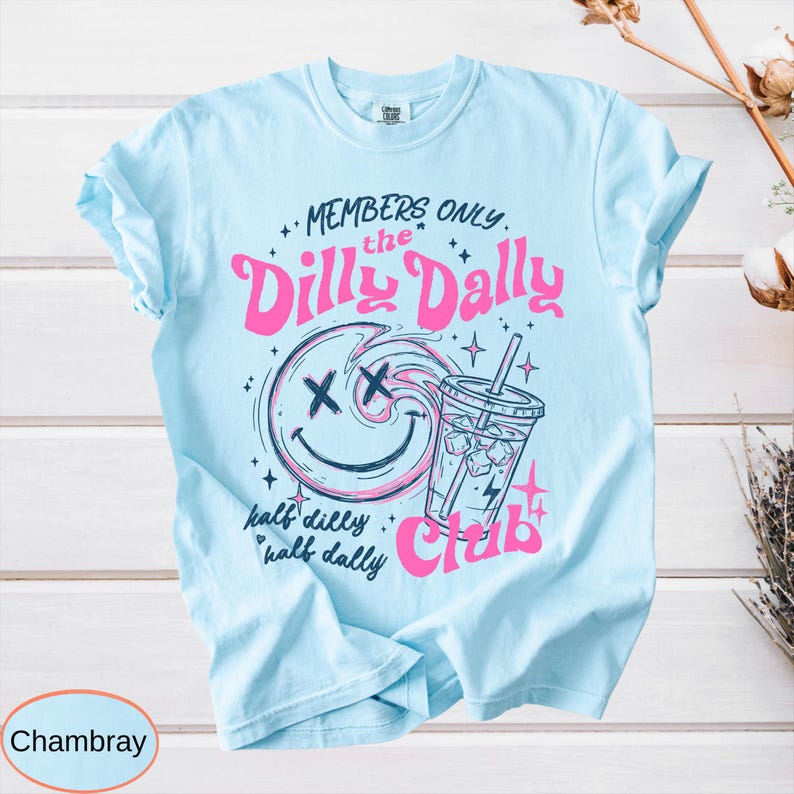 May include: Light blue t-shirt with the text "MEMBERS ONLY the Dilly Dally Club" in pink. The design includes a smiley face with an X for eyes, a drink, and the words "half dilly half dally".
