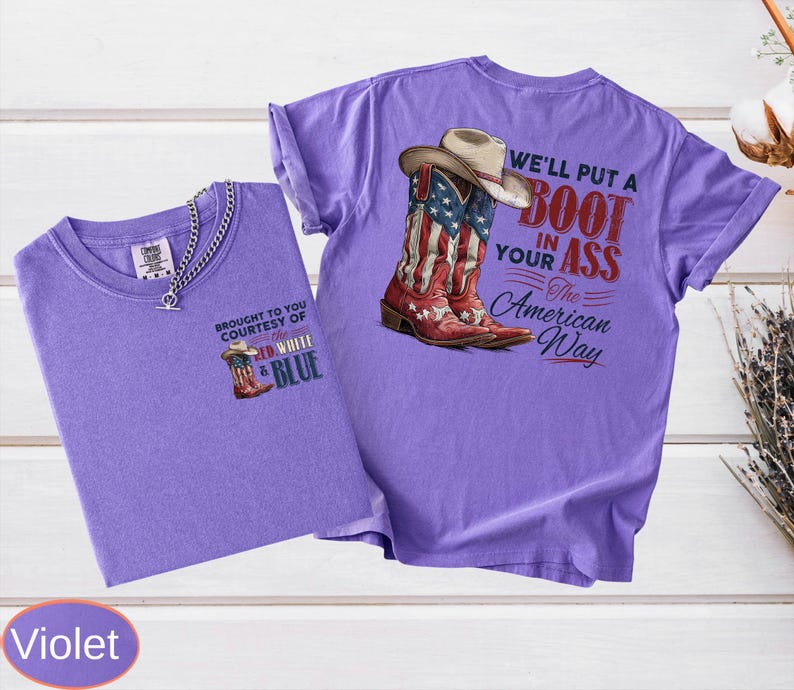 May include: Two violet t-shirts. One shirt has a small graphic of a cowboy boot with the text "BROUGHT TO YOU COURTESY OF RED WHITE & BLUE". The other shirt has a graphic of a cowboy boot with the American flag and the text "WE'LL PUT A BOOT IN YOUR ASS The American Way".