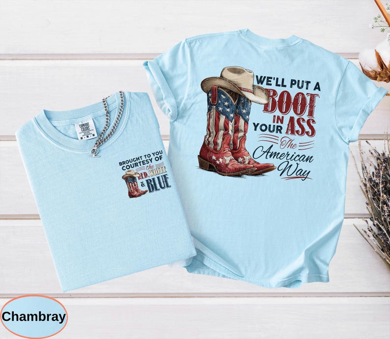 May include: Two light blue t-shirts. One features a graphic of a cowboy boot with the American flag design and the text "BROUGHT TO YOU COURTESY OF THE RED, WHITE & BLUE". The other shirt has a similar graphic of a cowboy boot and a hat with the text "WE'LL PUT A BOOT IN YOUR ASS The American Way".