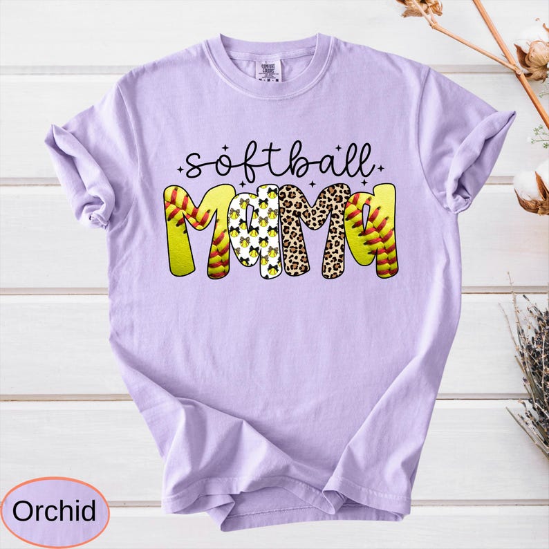 May include: Orchid-colored t-shirt with the words "softball mama" in a playful design. The word "softball" is in black script, and "mama" is in a mix of softball and leopard print patterns. A great gift for a softball mom.