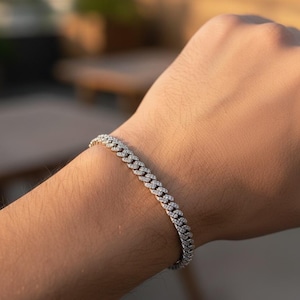 May include: A silver bracelet with a linked chain design, encrusted with small, sparkling stones. The bracelet is shown on a person's wrist, with a blurred background.