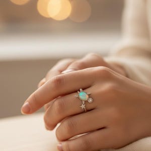 Op de afbeelding: Een zilveren ring met een schildpadontwerp, met een ovale opaal en diamantaccenten. De ring heeft een stervormig accent. De ring wordt op een hand getoond.