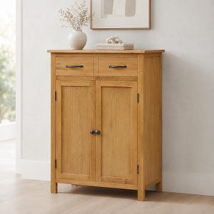 May include: A light brown wooden cabinet featuring two top drawers with horizontal black metal handles and two lower cabinet doors with round black knobs. The piece has a rectangular frame with visible wood grain and four sturdy legs.
