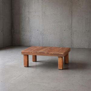May include: A rectangular, low-profile wooden coffee table. The table has a natural wood finish with visible grain and is supported by four sturdy, square legs. The design is simple and rustic, suitable for a living room or lounge area.