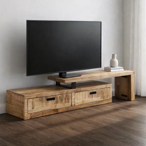 May include: A light-colored wooden TV stand with two drawers and a shelf. The stand supports a large black flat-screen TV. A small white vase and books are on the shelf. The stand is made of wood with a natural finish.
