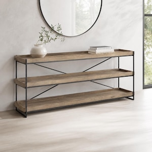 May include: A long console table with three rectangular wooden shelves and a black metal frame featuring X-shaped side supports. A white ceramic vase with a plant branch and a stack of three books are placed on the top shelf of the furniture.
