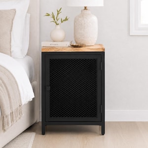 May include: A black metal nightstand with a rectangular wooden top and a single door featuring a diamond-patterned mesh screen. The nightstand has four straight legs and a small square handle on the left side of the door frame.