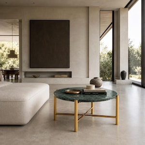 May include: A round coffee table featuring a dark green marble top supported by a gold-toned metal frame with four legs and a cross-brace base. The table surface holds a small gold tray, a stack of two books, and a small cylindrical container.
