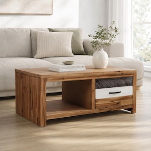 May include: A rectangular wooden coffee table with a natural finish. It features a drawer with a white front and a black handle, and an open shelf. The table is in a living room setting with a sofa and decorative items.