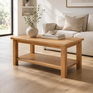 May include: A rectangular wooden coffee table with a lower shelf. The table is light brown and has a natural wood grain. A vase with greenery, books, and a small bowl are on top. The table is 48 inches long, 24 inches wide, and 18 inches high.