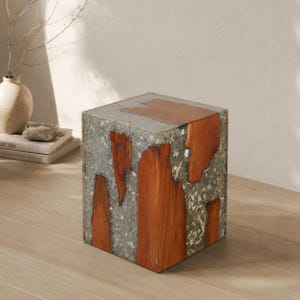 May include: A cube-shaped side table with a unique design. The table features a gray, speckled exterior with sections of warm, reddish-brown wood. The top of the table is also made of the reddish-brown wood. This accent table is a modern home decor item.
