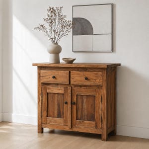 May include: A wooden cabinet with two drawers and two doors. The cabinet is made of light brown wood and has black knobs. A vase with dried branches and a small bowl sit on top of the cabinet. A framed abstract artwork hangs on the wall.