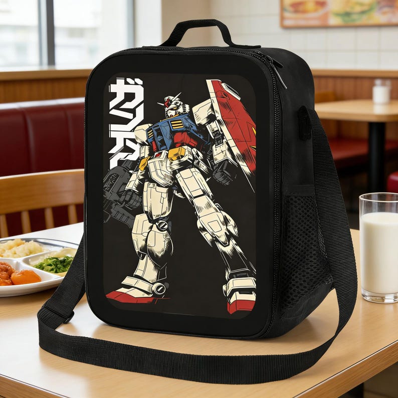 May include: Black lunch bag featuring a colorful illustration of a robot with the Japanese text "ガンダム" in white. The bag has a black shoulder strap, a top handle, and a side pocket. The robot is in shades of red, blue, yellow, and white.