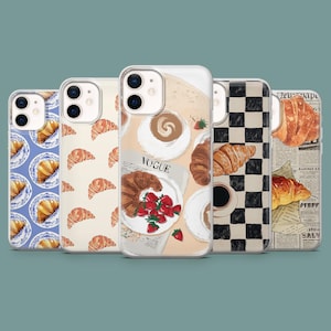May include: A collection of phone cases with various designs. One case features a blue plate with croissants, another has repeating croissants, and a third showcases a coffee and strawberry arrangement with the word "VOGUE". The fourth case has a black and white checkerboard pattern, and the last one has a newspaper print.