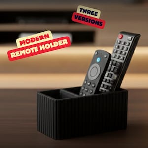 Könnte beinhalten: Ein schwarzer, moderner Fernbedienungshalter mit zwei Fächern, der zwei schwarze Fernbedienungen hält. Der Halter hat ein geripptes Design. Der Text auf dem Bild lautet "MODERN REMOTE HOLDER" und "THREE VERSIONS".