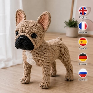 Pode incluir: Uma figura de bulldog francês em crochê feita de fio castanho-claro com focinho preto, orelhas grandes e eretas com detalhes cor-de-rosa no interior e uma mancha branca no peito. O brinquedo tem olhos escuros e redondos e um nariz preto.