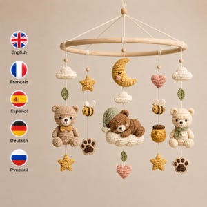 Pode incluir: Um móbile de berço com uma estrutura circular de madeira e elementos de crochê pendurados, incluindo dois ursinhos, um urso a dormir numa nuvem, uma lua crescente amarela, estrelas, corações, abelhas, potes de mel, pegadas e folhas verdes.